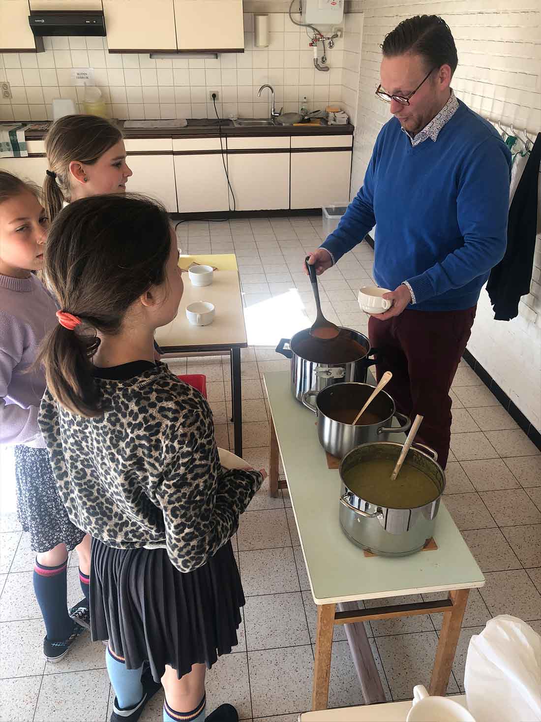 De voorzitter van het oudercomité schenkt soep uit aan enkele kinderen van het vijfde